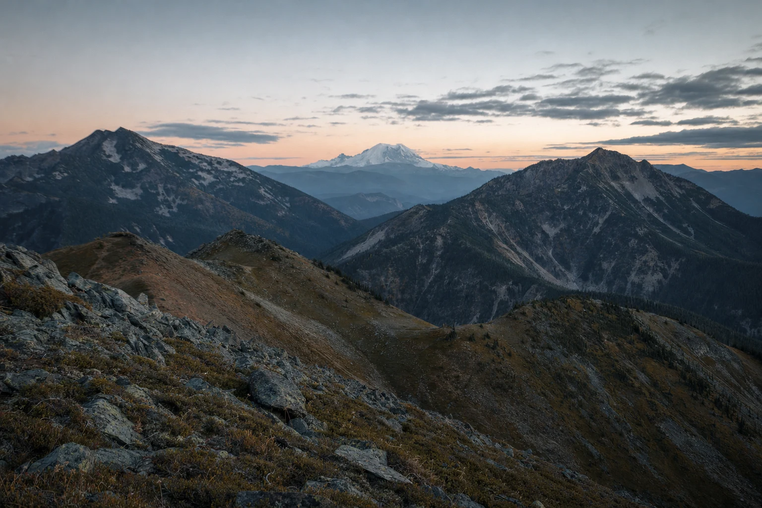 Three ridgelines converge toward a distant snow peak in cool dawn light.