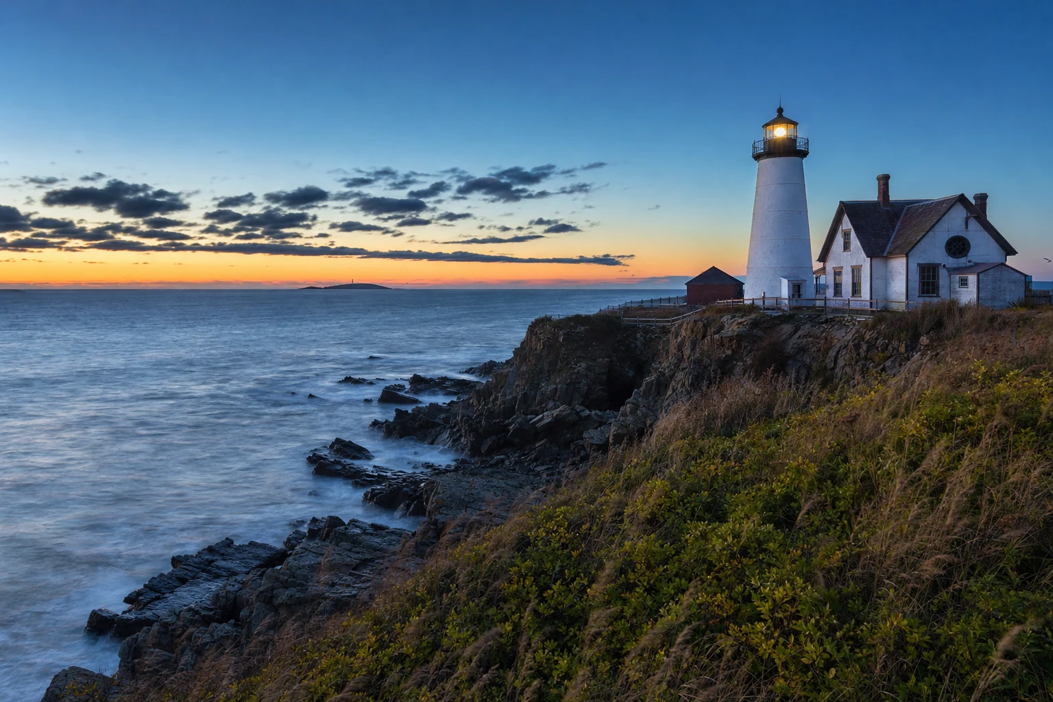 A welcoming coastal lighthouse stands on a grassy headland at blue hour with layered sea and sky in a calm editorial landscape.