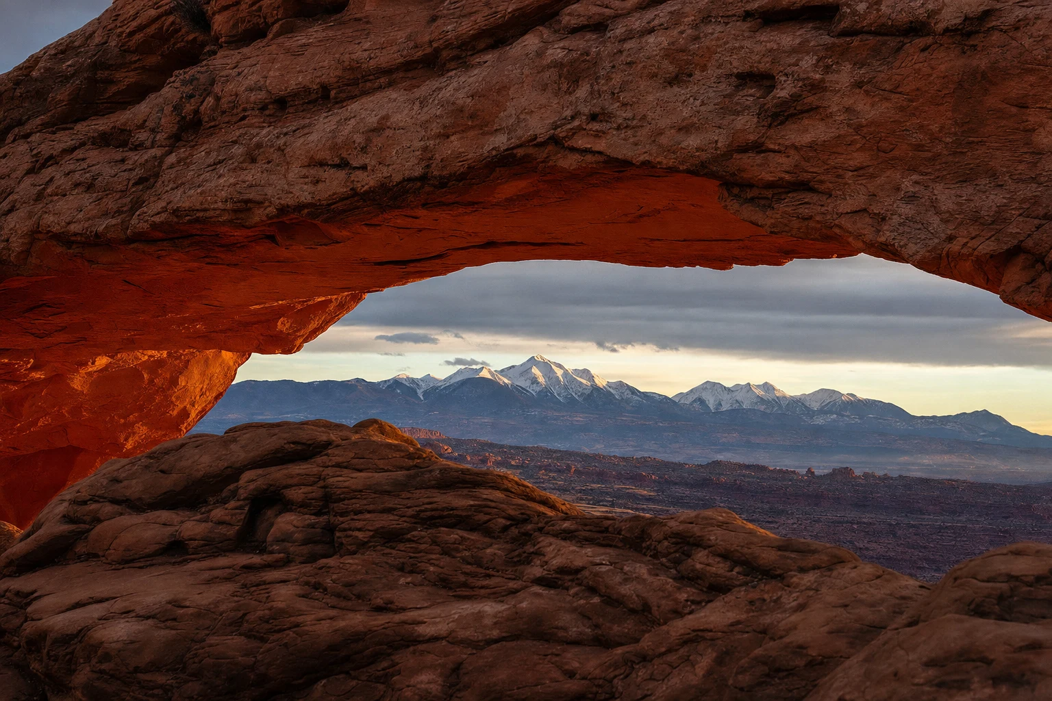 Un arco desértico color ámbar enmarca una lejana cordillera azul con luz natural