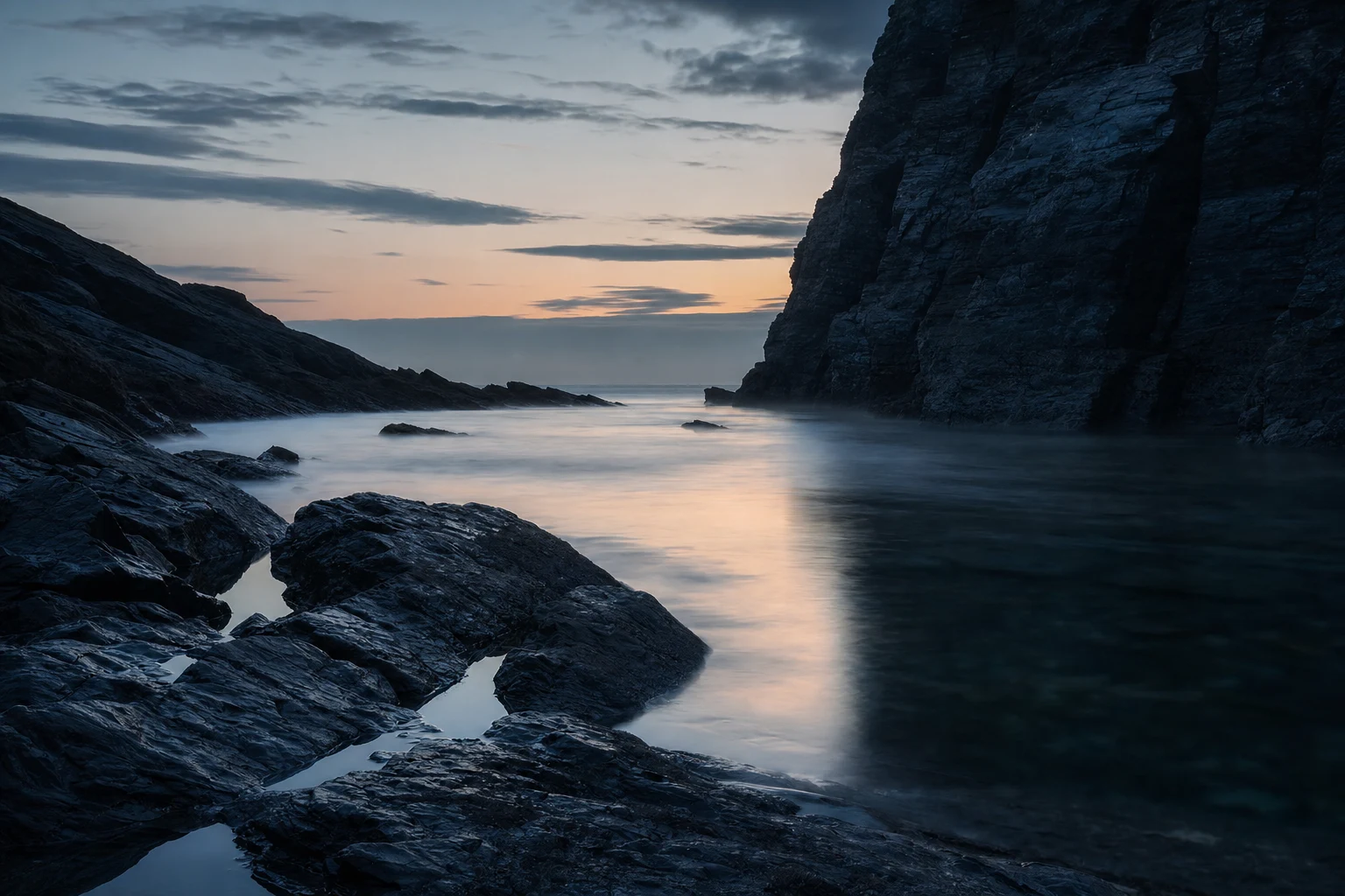 A still harborless cove before sunrise with calm water and dark cliffs.