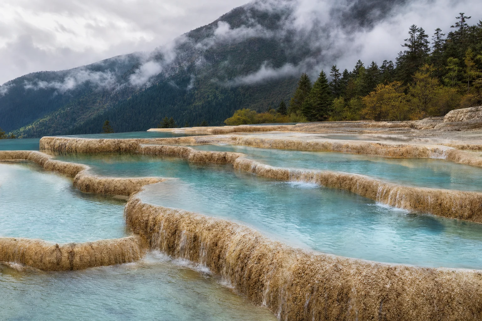 Stepped limestone pools with clear flowing water beneath soft overcast light, framed as a natural landscape editorial image.