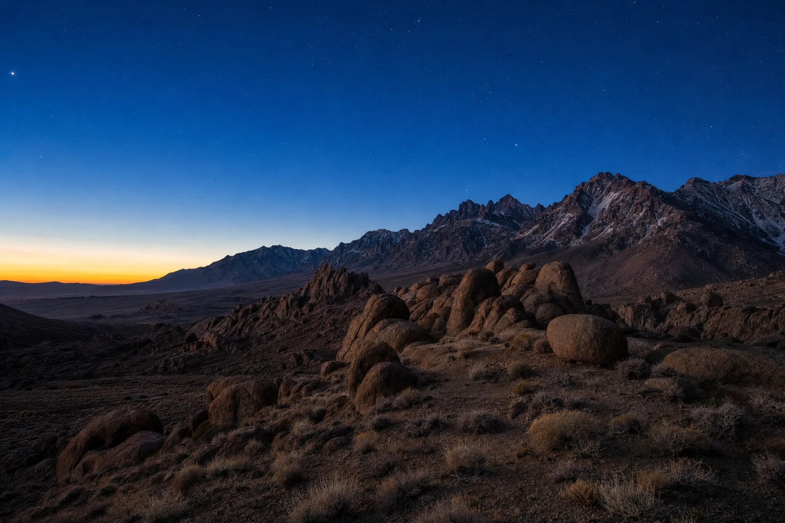 A wide photorealistic view of desert mountains under a deep blue sky just before dawn, with layered ridgelines and subtle atmospheric light.