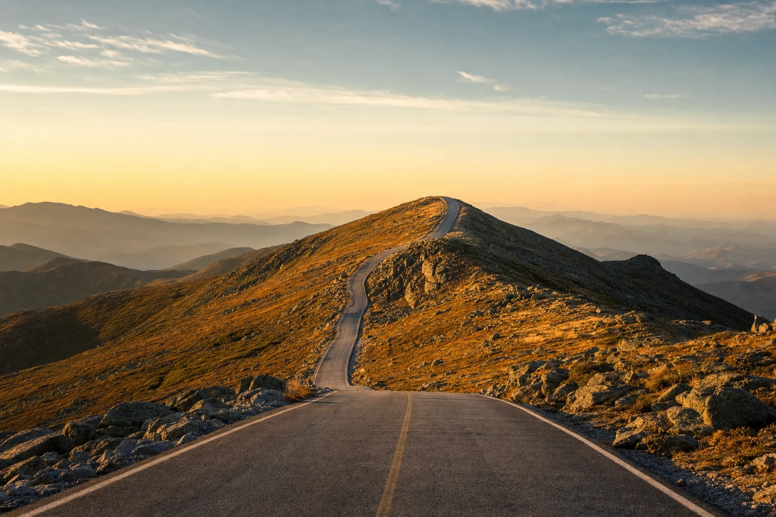 A quiet mountain road leading to a clear summit under golden light with layered natural landscape and no visible signage.